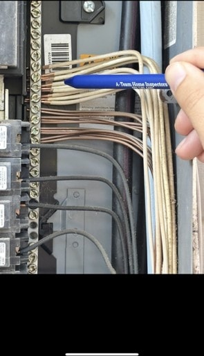Open electrical panel with two conductors clamped under a single terminal screw on the bus bar.