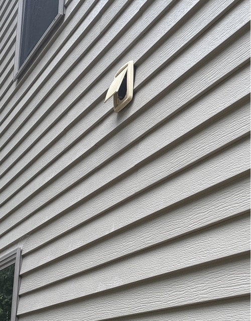 Exterior bathroom exhaust vent cap on vinyl siding with the weighted damper flap open and discharging correctly, on a Benton, Arkansas home.