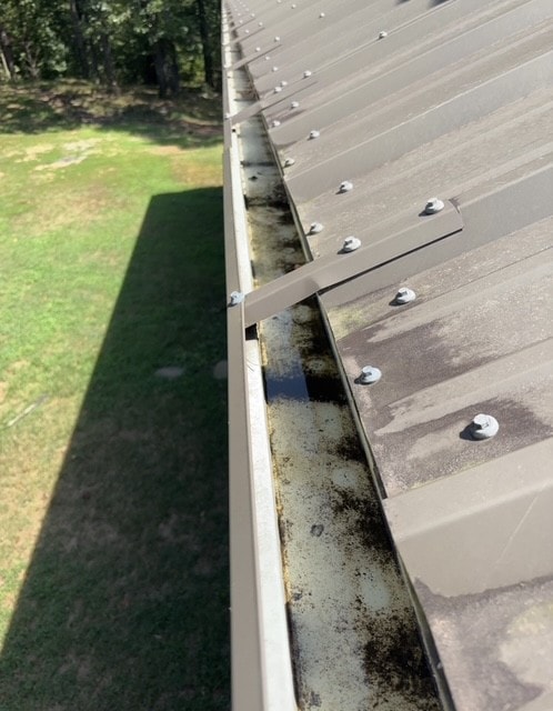 Seamless metal gutter along a metal roof edge, secured by a rigid hanger strap spanning the trough.