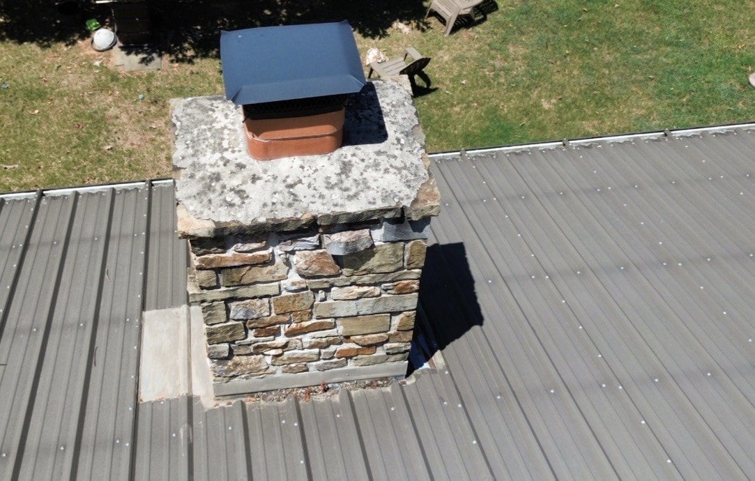 Aerial view of a stone chimney on a metal roof with no cricket or saddle built behind the high side.