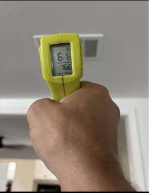 Infrared thermometer being aimed at a white ceiling supply register to measure air conditioning supply air temperature.