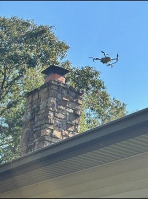 Inspection drone hovering above a stone chimney cap during an aerial roof survey.