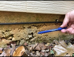 Exposed concrete foundation stem wall with pockmarked, spalling surface where the protective coating has failed.